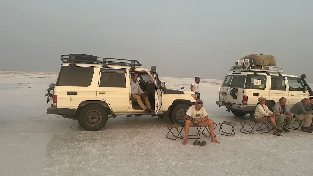 Travelers resting beside expedition vehicles at Lake Asale